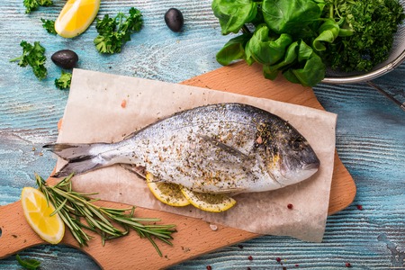 Cooking Raw Dorado Fish with Spinach, rosemary, olives, Herbs, Spices and Lemon closeup on Wooden...