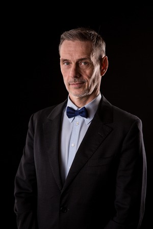 The older businessman in a suit with a bow tie on black background