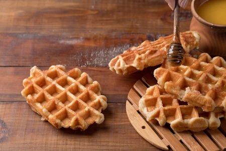 Honey pouring on a fresh waffles. Breakfast with waffles. Wooden background. Hand puts honey on wafflesの写真素材