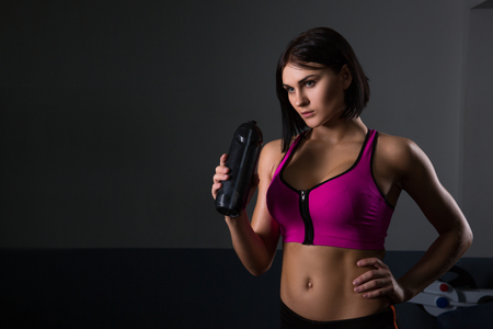 Young beautiful sportive girl drinking water over dark background. Halthy concept. Fitnessの写真素材
