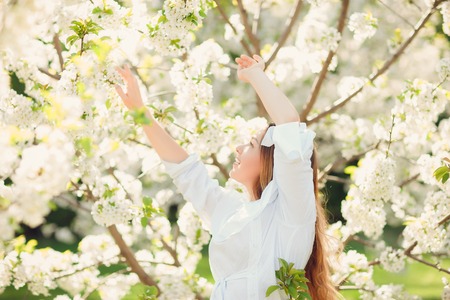 Young beautiful blonde woman in blooming almonds garden with white flowersの写真素材