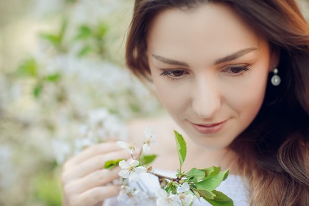 Young beautiful blonde woman in blooming almonds garden with white flowersの写真素材