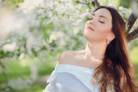 Close up romantic portrait of beautiful elegant woman in blossom spring trees. romantic mood surrounded by flowersの写真素材