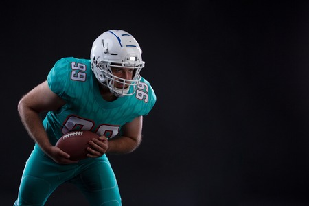 Portrait of American football player holding a ball in both his arms on black background. Copy space. Rugbyの写真素材