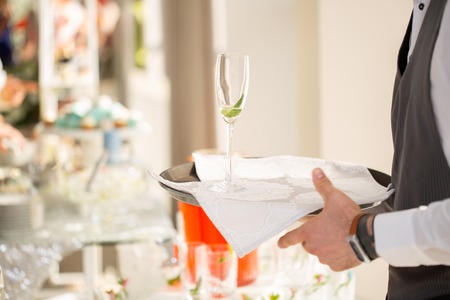 Waiter is holding a tray with glass of unfinished champagne on reception.