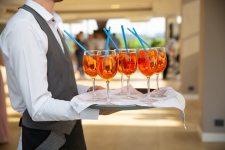 The waiter serves cocktails on a tray. Close-up orange and red cocktails with orange and mint at the restaurantの写真素材