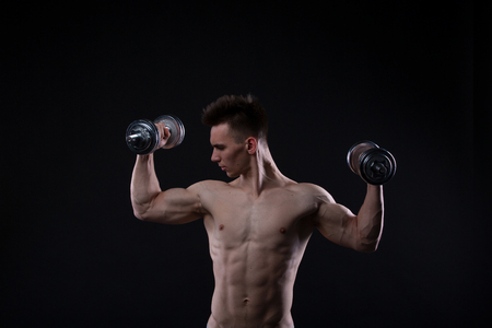 Muscular bodybuilder guy doing exercises with dumbbells over black backgroundの写真素材