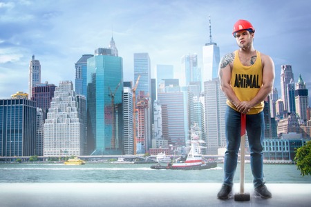 Sexy builder worker in helmet with hammer against the background of skyscrapers. Copy spaceの写真素材