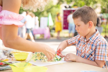 Cute little boy cutting shapes out of colored paper. Being creative, developing imagination,...