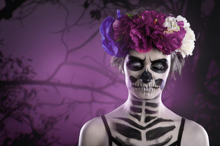 attractive woman with sugar skull make-up in front of creepy forest scene with full moon. Copy space