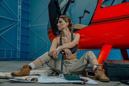 helicopter maintenance femail worker. woman pilot or helicopter mechanic holding the adjustable wrench. woman is tired after work. scattered drawingsの写真素材