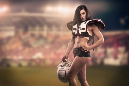 Athletic female dressed as an American Football Player at the stadium. Real uniform, helmet, pads, ball.の写真素材