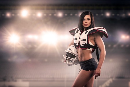 Athletic female dressed as an American Football Player at the stadium. Real uniform, helmet, pads, ball.の写真素材