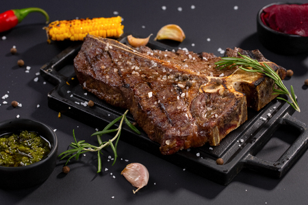T-bone beef stake served on a cutting board with sauces, rosemary, corn grillの写真素材