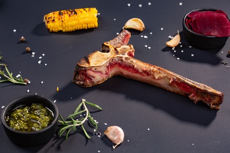 Gourmet Grill Restaurant Steak Menu - eaten T-Bone Beef Steak on black Background. Black Angus Prime Beef Steak. Beef Steak Dinner. gnarled bone with grilled corn, garlic, rosemary, sauces. finished dinnerの写真素材