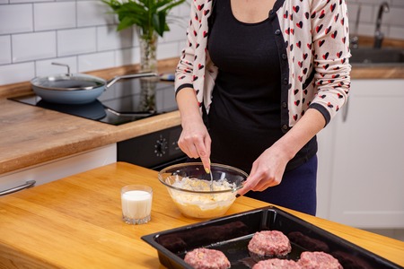 Young woman mixing cheese dough with a spoon in kitchen.の写真素材