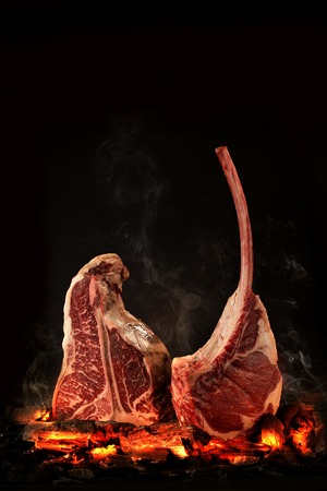 Whole T-Bone steak cooking on embers. Black background. Space for textの写真素材