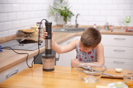 Cute toddler boy using hand blender to make minced meat. Preparing meal in the kitchen. Little boy learns to cookの写真素材