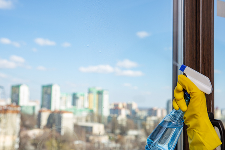 Female hand in yellow gloves cleaning window with spray detergent. Spring cleanup, housework conceptの写真素材