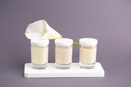 Luxurious cosmetic background. Candle Cream in three jars with white flower kala on grey background....
