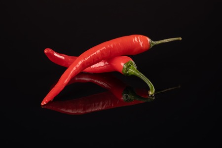Studio shot of group of red chilli peppers on a black background with mirror imageの写真素材