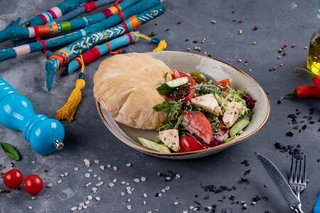 Greek salad with fresh cherry tomatoes, feta cheese, black olives, basil and onion on black stone background, pancake. Dish decorated with spicesの写真素材