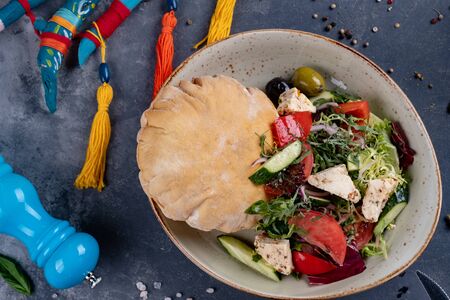 Greek salad with fresh cherry tomatoes, feta cheese, black olives, basil and onion on black stone background, pancake. Dish decorated with spicesの写真素材