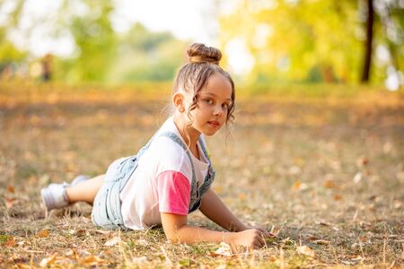 A front portrait of a little girl lying on a colorful leaves in autumn parkの写真素材