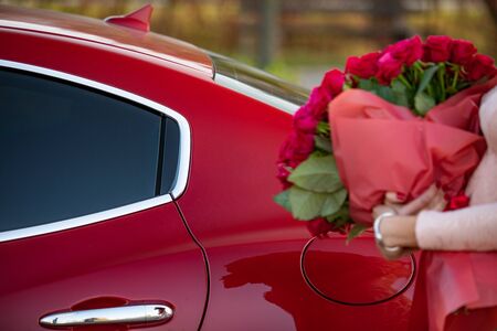 Woman near the car with beautiful bouquet of roses in hands.の写真素材