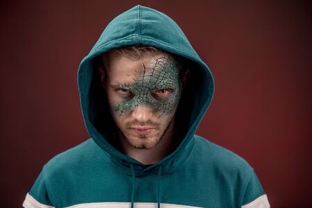 Man with professional horror movie make-up green lizard on dark red
