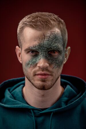 Man with professional horror movie make-up green lizard on dark redの写真素材