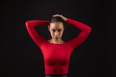 Young woman tying up her long brunette hair in a a ponytail neatening it with her hands on black backgroundの写真素材