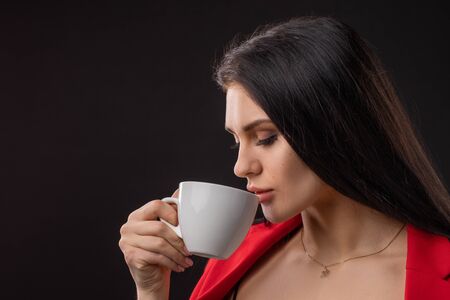 Beautiful happy woman drinking a cup of coffee on black backgroundの写真素材