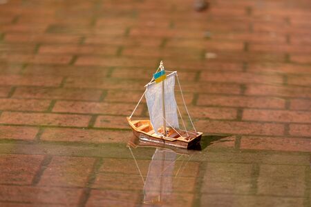 Spring. hand starts A wooden toy boat with a sail from medical gauze mask swims along a city puddle. the flag of Ukraine is set on the mast. sail of hope for virus protectionの写真素材