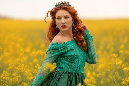 Beautiful Redhead female model in a field of yellow rapeseed flowers.の写真素材