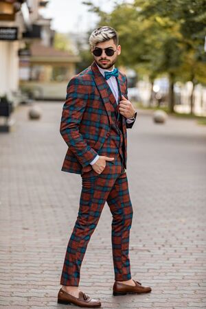 Handsome young businessman checking time on his wristwatch. Man wearing at the luxery check suit walking on the streetの写真素材