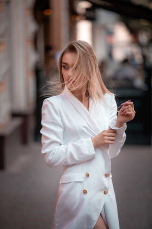 portrait of fashionable blonde wearing at white jaket or blazer in the city, developing hair. Street photoの写真素材