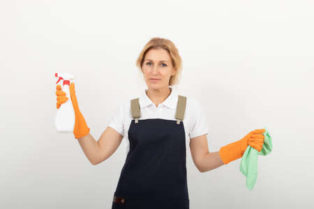A woman cleaning lady or houswife with a rag in her hand holds an air freshener spray. House cleaning concept or office cleaning concept on light background. A woman wearing an apron. cleaning agency provides its servicesの写真素材
