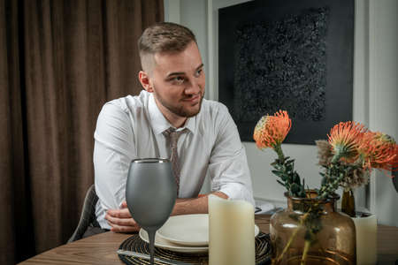 Portrait of a young handsome man sitting at the table during romantic dinner at homne