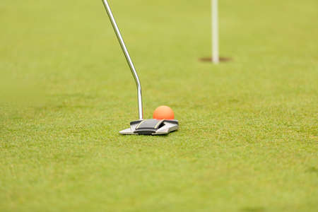 putter golf club hammering a golf ball into a holeの写真素材