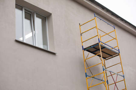 Outside repair and renovation of a apartment house using blue paint metal small scaffolding tower....
