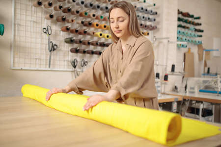 Woman rolls a roll of yellow material. The roll of material lies a light table.
