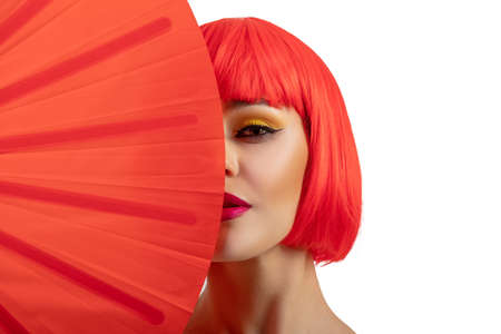 Beautiful girl wearing short red wig holding red fan isolated on white background. Half faceの写真素材