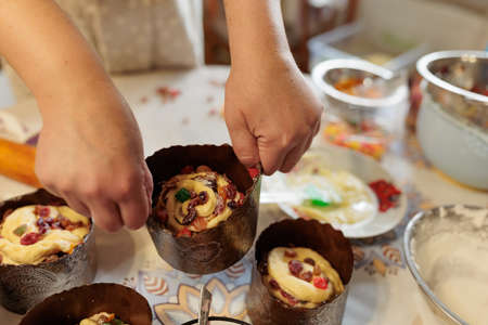 a woman cook lays out dough with candied fruits in paper molds for baking Easter cakes. family...