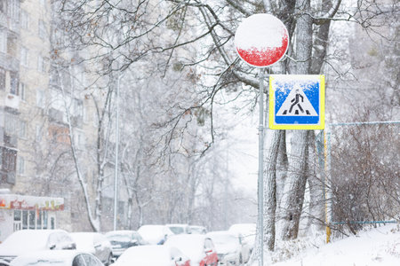 difficult road conditions - road in the winter snowfall with pedestrian crossing sign covered by snowの写真素材