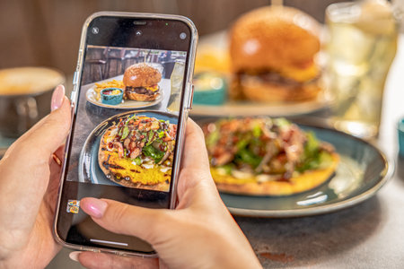 girl hand Taking photo og burger and meat on cellphone in restaurantの写真素材