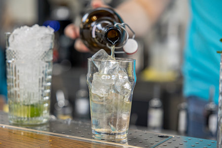 barman gently pours alcohol from a bottle into glass with ice.