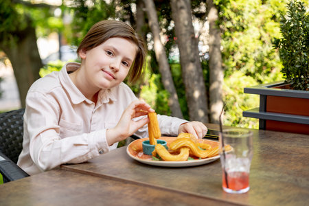 Portrait of teenager boy eating french churros in the outdoor summer cafeの写真素材