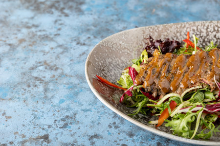 Sliced grilled beef steak with green leaves salad on rustic plate with cutlery. Medium rare barbecue steak and healthy salad on gray stone background, place for textの写真素材