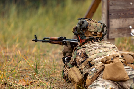 Ukrainian military soldier in a helmet and with machine gun shoots lying on the ground at a target at 100 meters. shooting at the range. shells on the ground.の写真素材